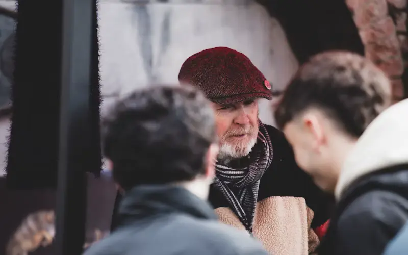 Close-up of an older man in a flat cap talking with someone outdoors